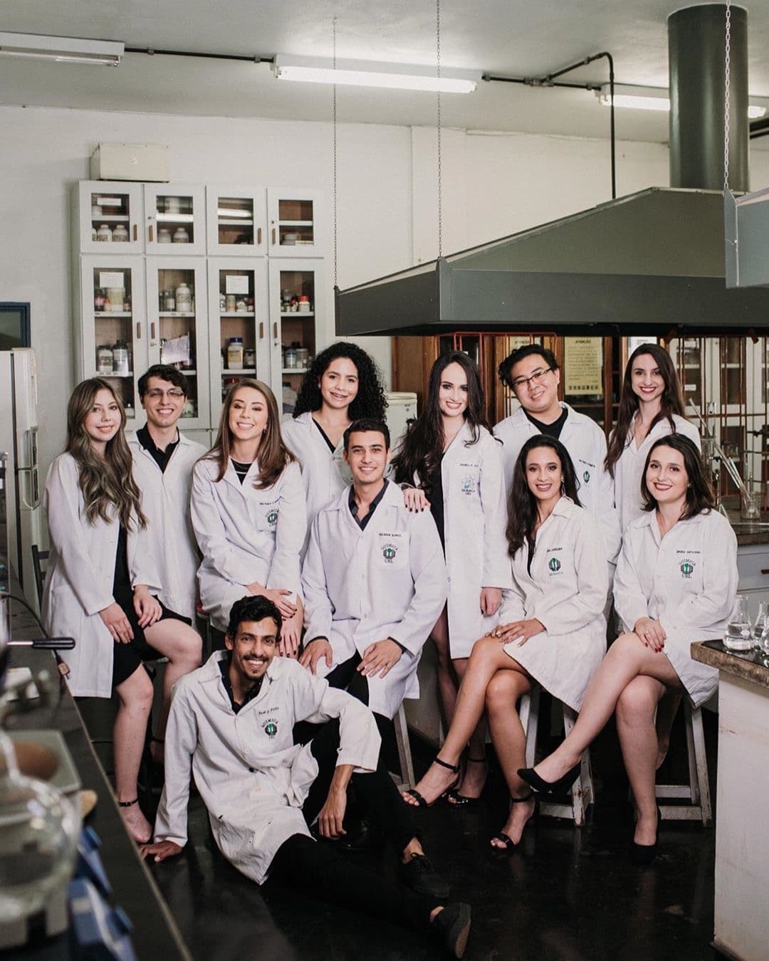 Turma de estudantes universitários usando jalecos brancos personalizados da Casa do Jaleco em laboratório