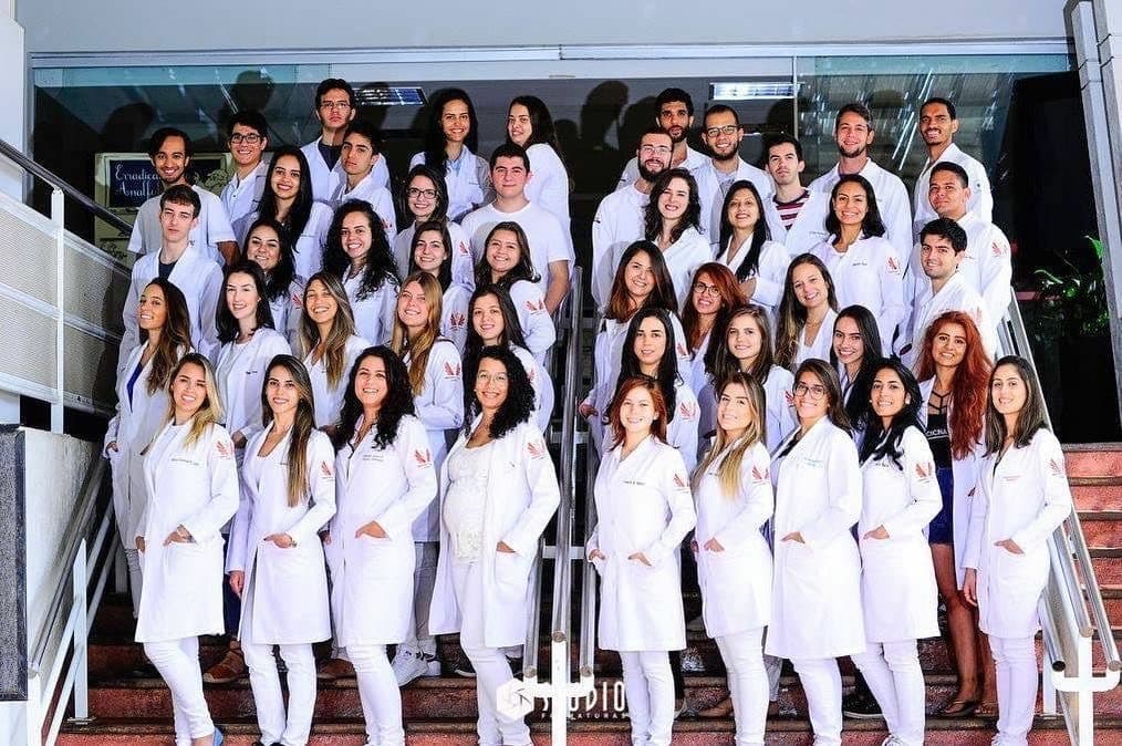 Grande turma de medicina com jalecos brancos personalizados na escadaria da faculdade